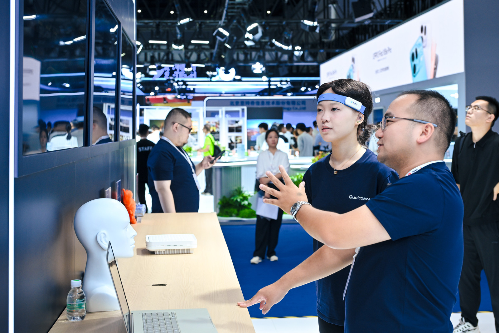 A visitor wears WABO Dreamer while staff explain the AI art experience at Qualcomm’s booth.
